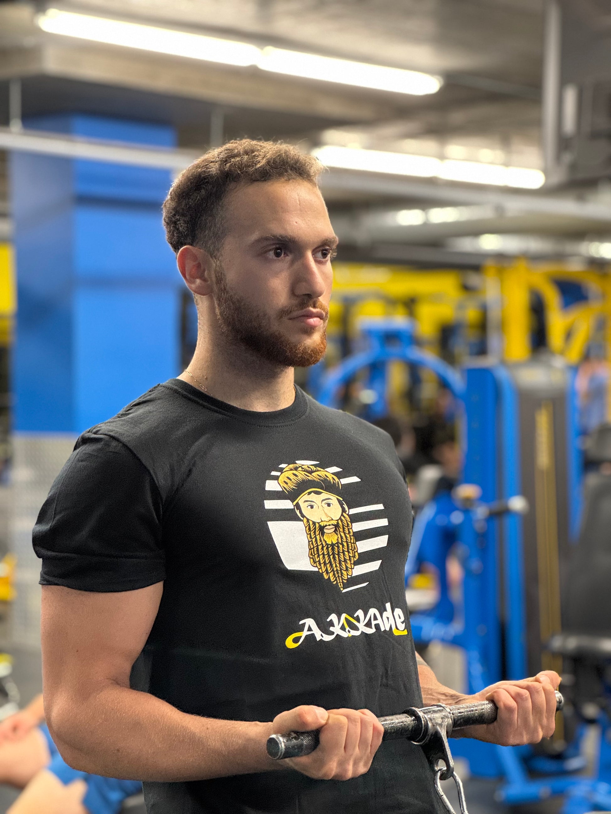 Man in a gym wearing a black t-shirt with Akkade logo, holding a barbell.